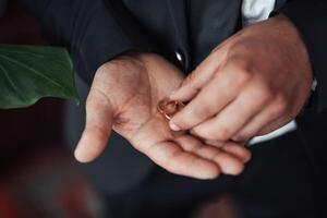 A man is holding a ring in his hand. The ring is gold and has a heart shape. The man is wearing a suit and tie, and the image has a formal and elegant mood photo