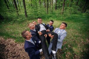 A group of men are playing in the woods, one of them is being lifted by the others photo