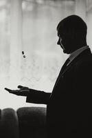 A man in a suit holding a ring in his hand. The man is wearing a tie and is standing in front of a window photo