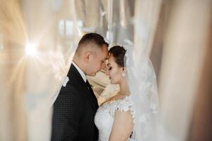 A bride and groom are embracing each other in a wedding photo. The bride is wearing a white dress and the groom is wearing a suit. The photo is taken from behind a curtain