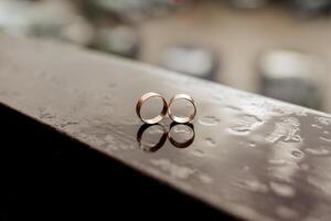 Two gold wedding rings are placed on a wet surface. The rings are reflecting the light, creating a beautiful and romantic atmosphere photo