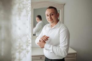 A man in a white shirt is standing in front of a mirror, adjusting his shirt. Concept of self-care and attention to detail, as the man takes the time to ensure his appearance is neat and tidy photo