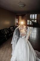 A bride and groom are posing for a picture in a room with a wooden floor. The bride is wearing a white dress and the groom is wearing a suit. Scene is happy and romantic photo