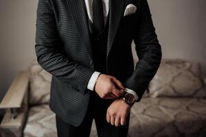 A man in a suit is wearing a watch and adjusting his tie. Concept of formality and professionalism, as the man is dressed in a suit and tie photo
