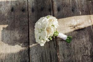 A bouquet of white flowers sits on a wooden table. The flowers are arranged in a vase and are the main focus of the image. The wooden table provides a rustic and natural backdrop for the flowers photo