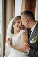A bride and groom are hugging and smiling at the camera. The bride is wearing a white dress and the groom is wearing a suit. Scene is happy and joyful, as the couple is celebrating their wedding day photo