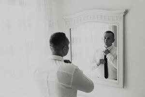 A man is getting ready for a wedding and is adjusting his tie in front of a mirror. Concept of formality and preparation for a special occasion photo