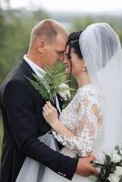 A bride and groom are hugging each other with a white veil on the bride's head. The bride is holding a fern in her hand photo