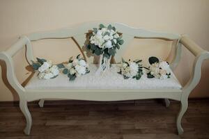 A white bench with a bouquet of flowers on it. The bench is placed in a room with a tan wall photo