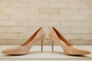 Two women's high heels are standing next to each other on a white surface. The heels are made of a shiny material and have a pointed toe. Concept of elegance and sophistication photo