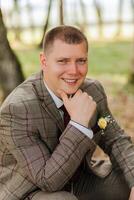 A man in a suit is sitting on the ground with his hands on his knees. He is smiling and looking at the camera photo