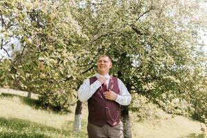 A man in a vest and tie stands in front of a tree. The man is smiling and he is enjoying the outdoors. Concept of relaxation and happiness photo