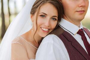 A bride and groom are posing for a picture, with the bride wearing a white veil and the groom wearing a red vest. Scene is happy and romantic, as the couple is embracing and smiling for the camera photo