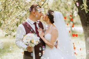 A bride and groom are hugging in a park, with the bride holding a bouquet of flowers photo