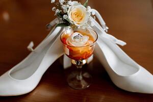 A pair of white shoes with a rose on them and a glass of wine. Concept of elegance and sophistication, as the shoes photo