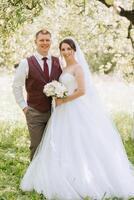 A bride and groom are posing for a picture in a field. The bride is wearing a white dress and the groom is wearing a red vest photo