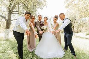 A group of people posing for a picture, including a bride and groom. The bride is wearing a white dress and the groom is wearing a suit. The group is standing in a grassy field photo