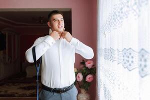 A man in a white shirt is getting dressed and adjusting his tie. Concept of formality and preparation for a special occasion photo