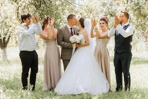 A group of people are posing for a picture, with a bride and groom in the center. The bride is wearing a white dress and the groom is wearing a tie photo