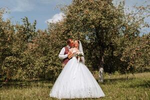 A bride and groom are standing in a field of apples, with the bride wearing a white dress and the groom wearing a vest photo