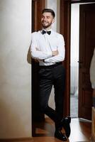 A man in a suit and tie stands in front of a door. He is smiling and he is confident photo