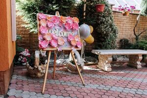 A sign with pink flowers and the word welcome on it is on a wooden stand. A balloon is next to the sign photo