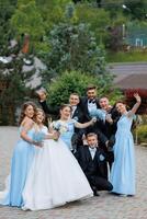 A group of people posing for a picture, including a bride and groom. The bride is wearing a white dress and the groom is wearing a suit. The group is smiling and he is happy photo