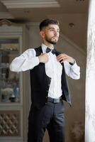 A man in a suit and vest is getting ready to go out. He is adjusting his tie and looking out the window. Concept of formality and preparation for a special occasion photo