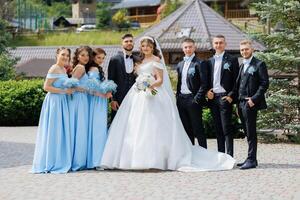 A bride and groom stand in front of a group of bridesmaids and groomsmen photo