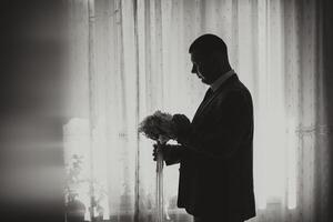A man in a suit is holding a bouquet of flowers. He is standing in front of a window, and the flowers are in a vase. Concept of elegance and sophistication photo