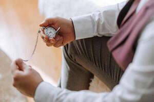 A man is sitting on a rug with a pocket watch in his hand. He is wearing a white shirt and a purple vest photo