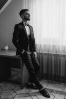 A man in a suit and tie is standing in front of a window. He is wearing a bow tie and has a serious expression on his face photo
