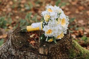 A bouquet of white and yellow flowers is sitting on a log. The flowers are arranged in a way that they are all facing the same direction, creating a sense of unity and harmony photo
