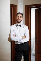 A man in a suit and tie is standing in front of a door. He is smiling and looking at the camera photo