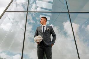 A man in a suit and tie stands in front of a large window, holding a bouquet of flowers. Concept of elegance and sophistication, as the man is dressed in a formal attire photo