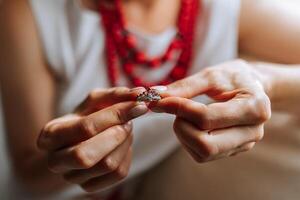 A woman is holding a ring in her hand. The ring is a diamond ring with a red band. The woman is wearing a white shirt and a red necklace. Concept of elegance and sophistication photo