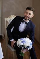 A man in a suit and tie is sitting on a chair with a bouquet of flowers in his lap. He is smiling and he is happy photo
