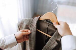 A man is holding a jacket on a hanger. The jacket is plaid and has a brown collar photo
