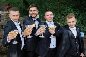 A group of men in suits are holding up glasses of champagne and smiling. Scene is celebratory and happy photo