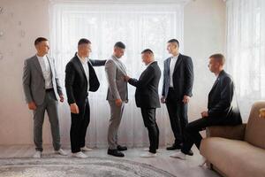 A group of men are dressed in suits and ties, with one man helping another adjust his tie. Scene is formal and professional, as the men are getting ready for a special occasion or event photo