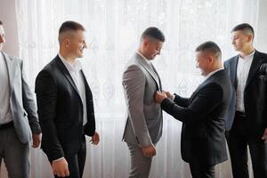 A group of men are getting dressed up for a wedding. One man is helping another man put on his tie photo
