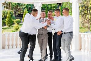 A group of men are standing together, one of them is wearing a tie. They are all smiling and seem to be enjoying each other's company photo