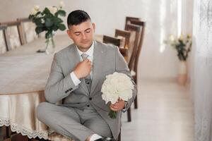 A man in a suit is sitting at a table with a bouquet of white flowers in his lap photo