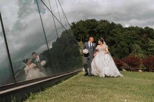 A bride and groom are walking together in a field. The bride is wearing a white dress and the groom is wearing a suit. They are holding hands and appear to be happy photo