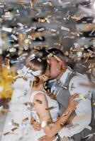 A bride and groom are kissing in the air with confetti falling around them. Scene is joyful and celebratory, as the couple is getting married photo