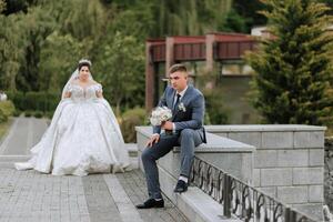 A bride and groom are standing in front of a building. The bride is wearing a white dress and the groom is wearing a suit. The bride is holding a bouquet and the groom is holding a bouquet as well photo
