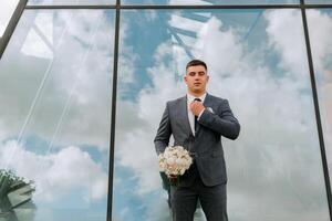 A man in a suit and tie stands in front of a large window, holding a bouquet of flowers. Concept of elegance and sophistication, as the man is dressed in formal attire photo
