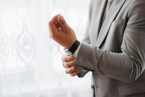 A man in a suit is getting ready to wear his watch. He is adjusting the watch band and making sure it is secure. Concept of formality and attention to detail photo