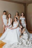 A group of women in white dresses pose for a photo. Scene is elegant and sophisticated, as the women are dressed in formal attire. The photo captures a moment of camaraderie