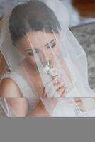 A bride is wearing a veil and holding a flower. The veil is made of a net-like material and covers her face. The bride appears to be in a state of contemplation or reflection photo